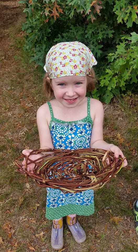 Child smiling outdoors while holding a handmade woven basket.