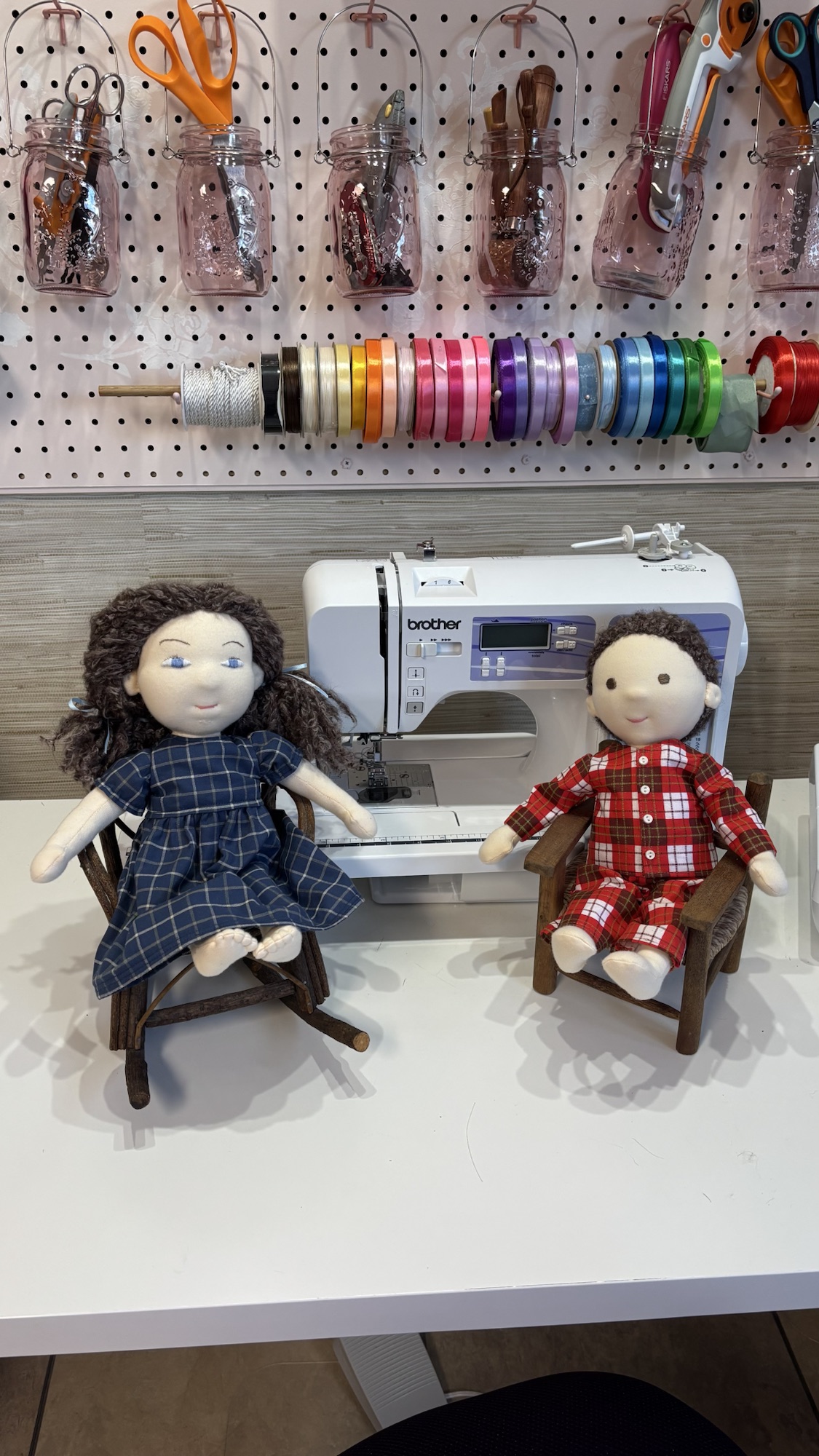 Two handmade cloth dolls seated beside a sewing machine.