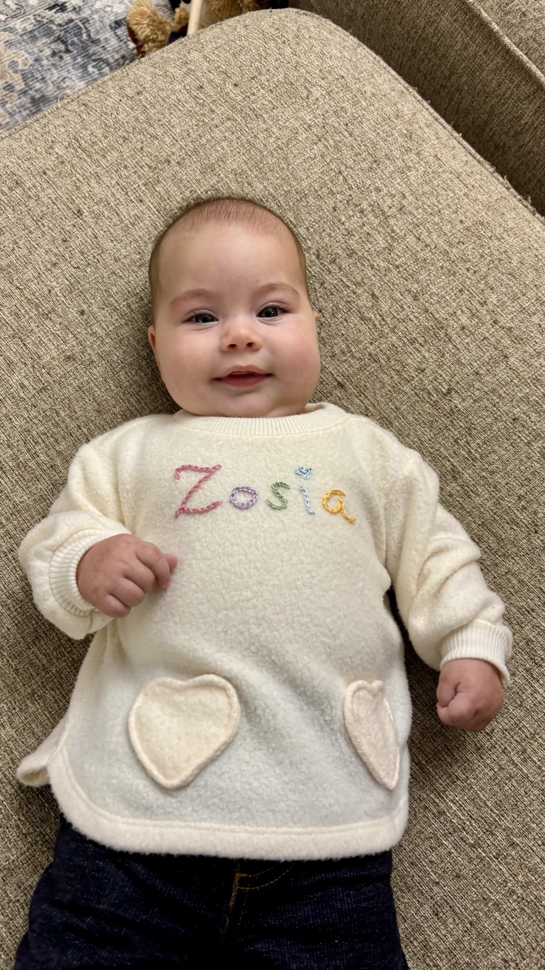 Baby wearing a handmade wool sweater with embroidered lettering and felt pockets.