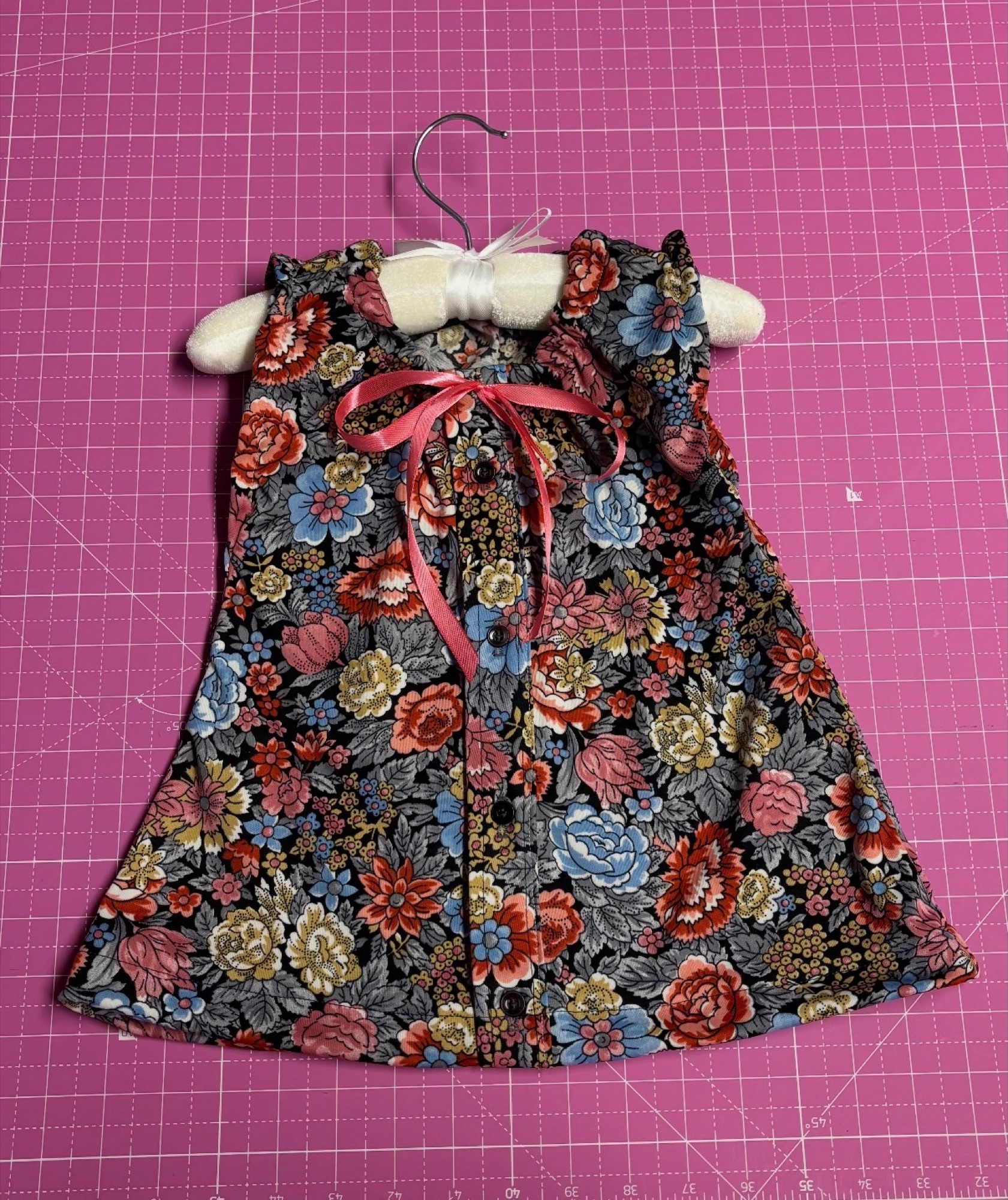 Handmade dark floral doll dress displayed on a small hanger.