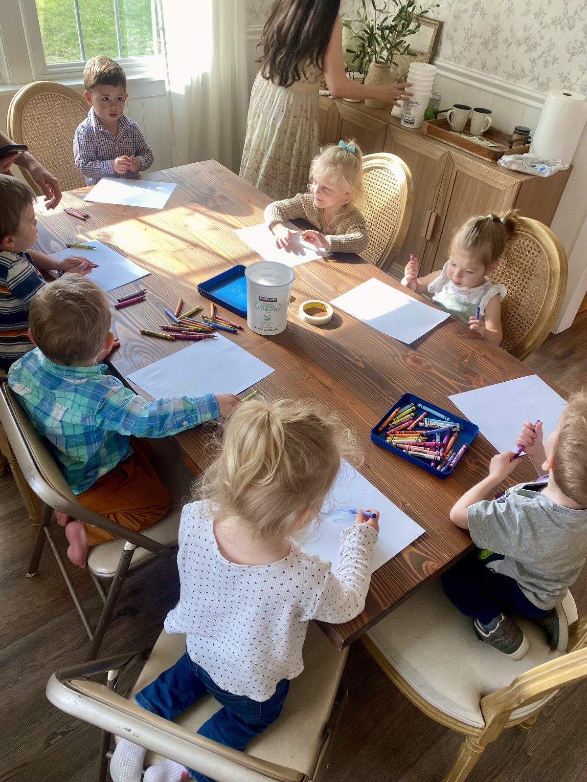 Children gathered around a table working on art projects in a home studio setting.