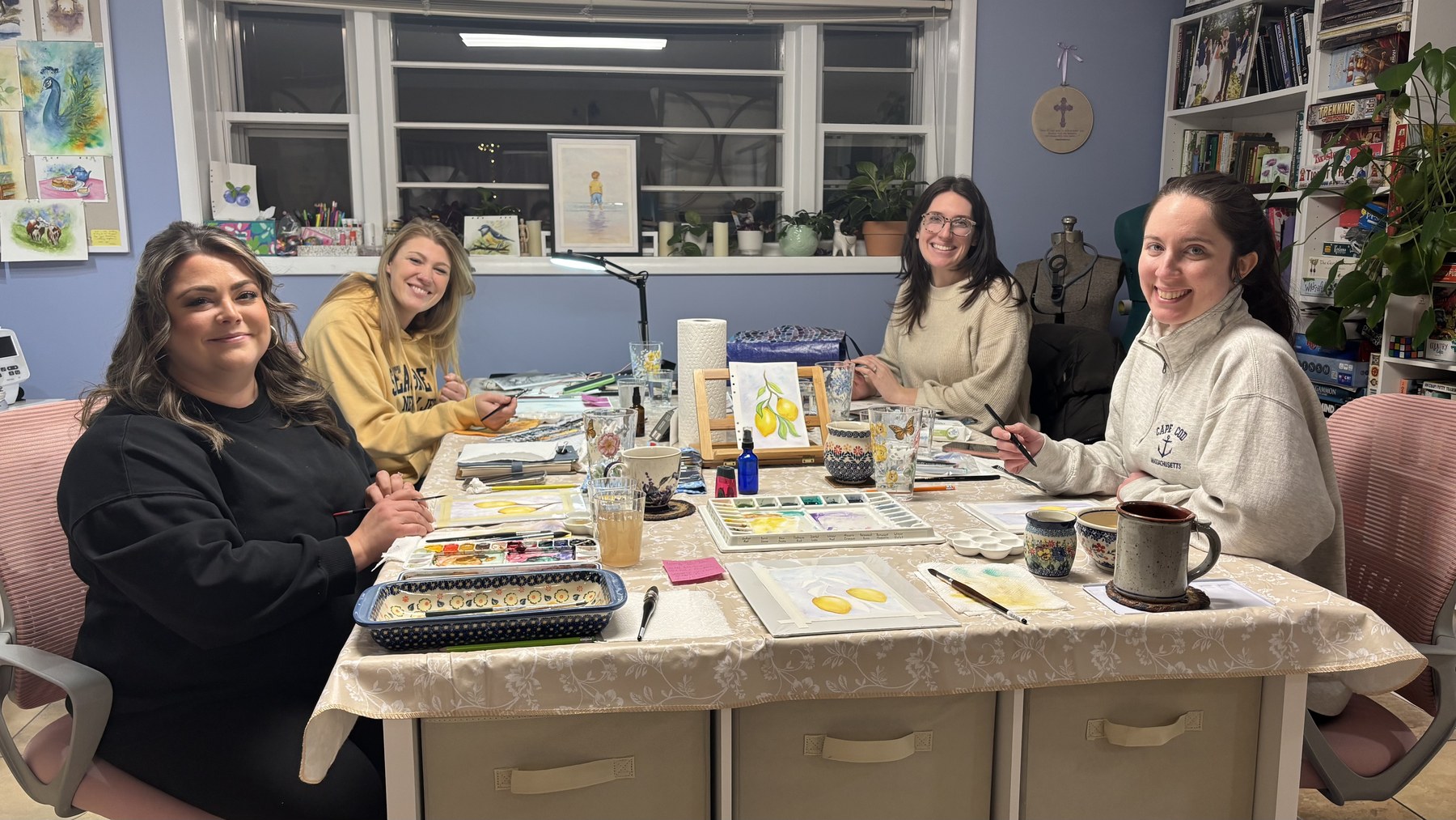 Adult students smiling around a table with watercolor supplies and artwork.